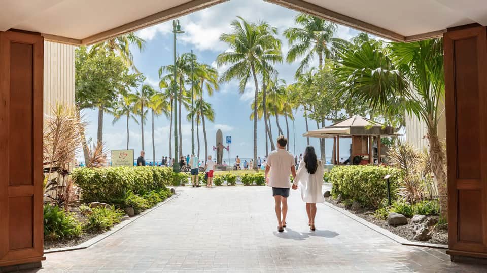 Couple jogging on beachfront promenade with palm trees and city skyline visible