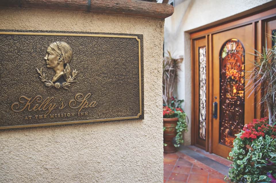 Bronze plaque for Kelly's Spa at the Mission Inn entrance with ornate wooden doors and flowers