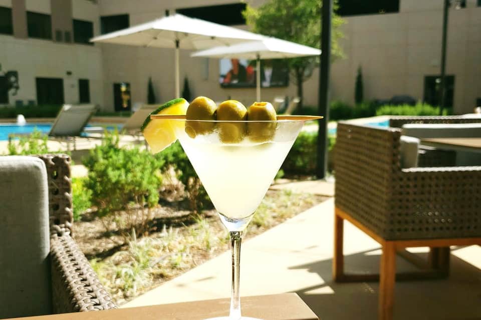 Martini cocktail with olives on a skewer at a poolside resort patio with umbrellas