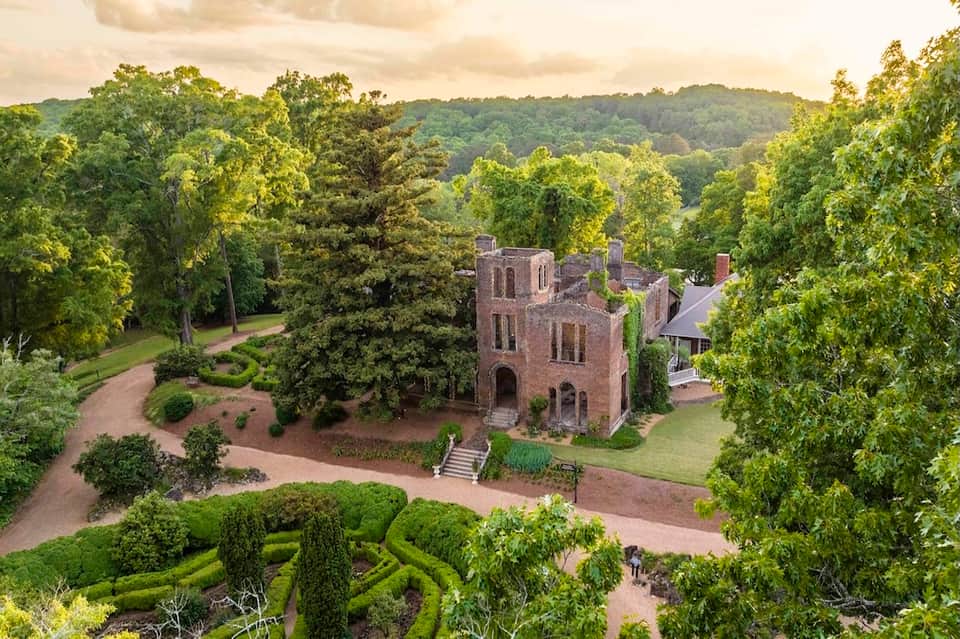 Aerial view of historic brick mansion surrounded by manicured formal gardens and lush forest landscape