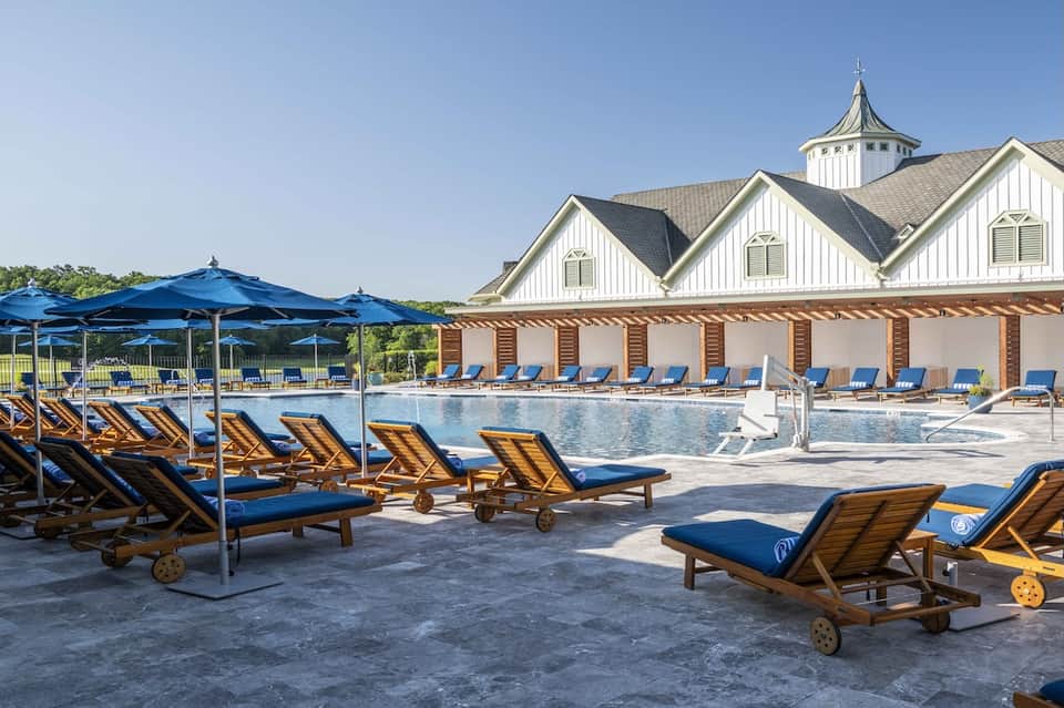 Resort pool with blue lounge chairs, umbrellas, and colonial-style pool house