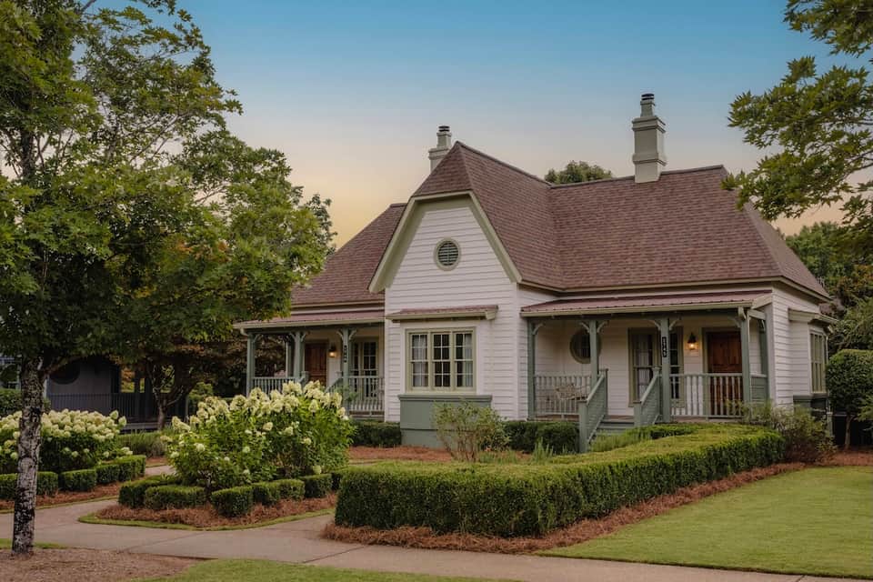 Charming cottage-style house with white siding, brown roof, and manicured landscaping