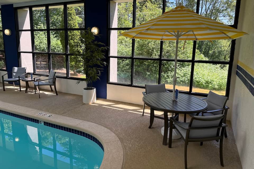 Indoor pool area with striped umbrella, dining table, large windows overlooking forest