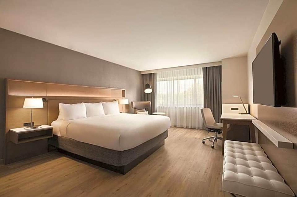 Contemporary hotel bedroom with queen bed, wood headboard, flat-screen TV, and work desk area