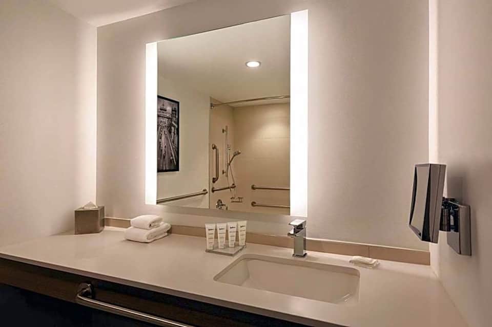 Luxury bathroom vanity with large illuminated mirror, white countertop, sink, and toiletries displayed
