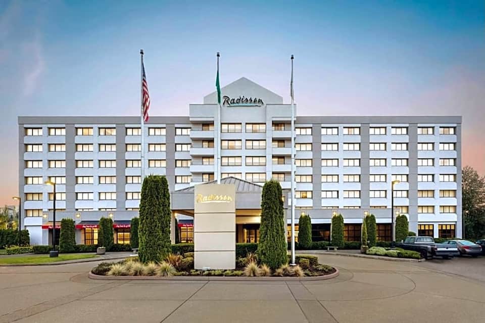 Radisson hotel exterior, multi-story white building with flags and landscaped entrance at dusk