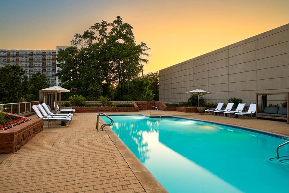 Resort swimming pool at dusk with lounge chairs, umbrellas, and sunset sky backdrop