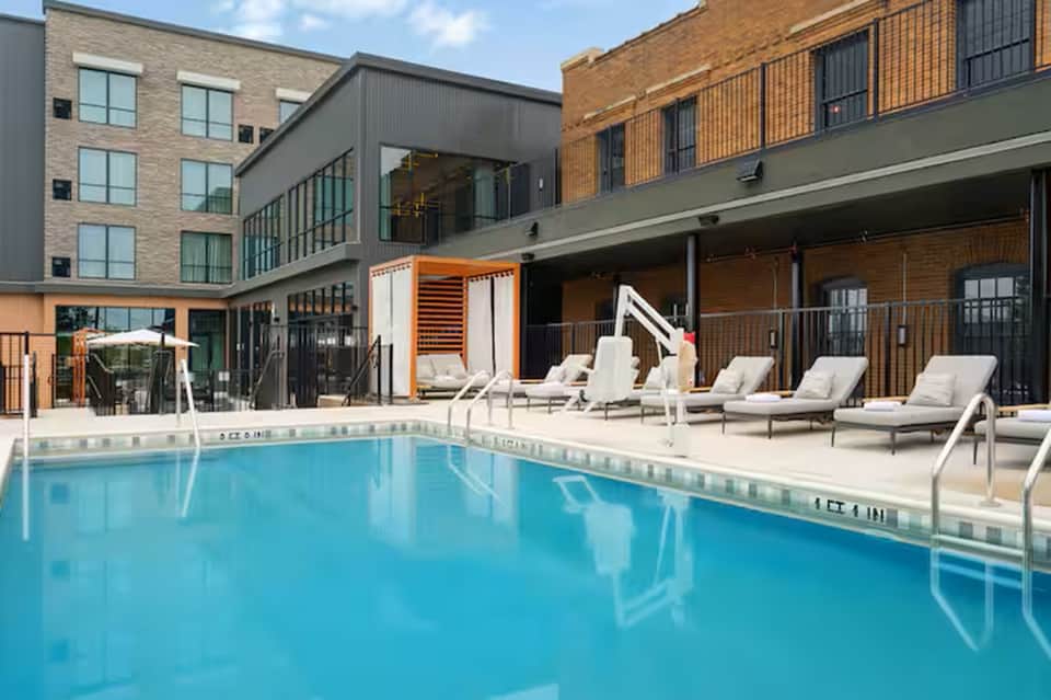 Resort pool surrounded by lounge chairs with modern brick and glass buildings