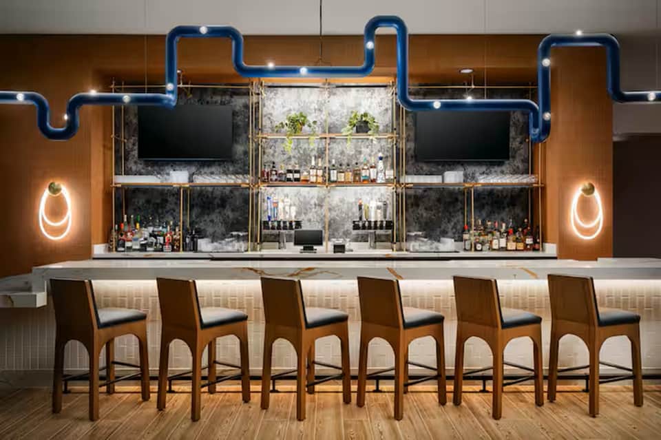 Modern bar with blue neon pipe design, wood paneling, multiple screens, and leather bar stools