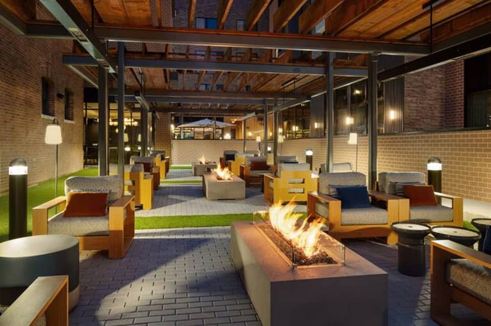 Modern covered outdoor patio with fireplace, lounge seating, exposed wooden beams, and ambient lighting