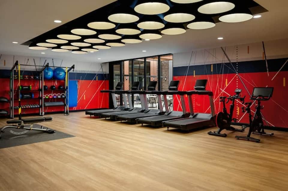Contemporary fitness center with treadmills, stationary bikes, red accent walls, and modern lighting
