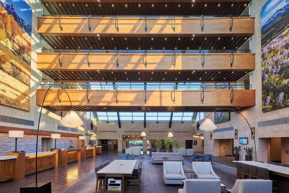 Grand hotel atrium with multi-level wooden balconies, natural skylight, contemporary furnishings, and vibrant artwork