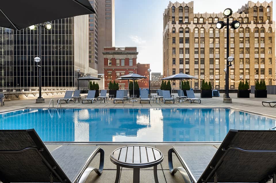 Urban rooftop pool with blue lounge chairs, umbrellas, and historic building architecture backdrop