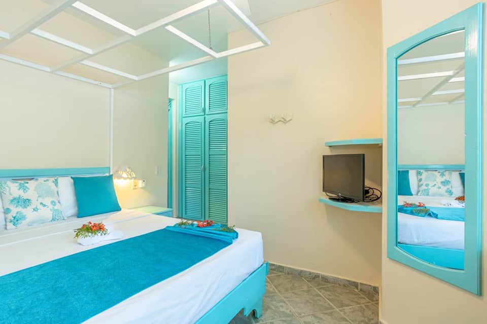 Colorful hotel room with turquoise accents, double bed, flat-screen TV, and bright ceiling