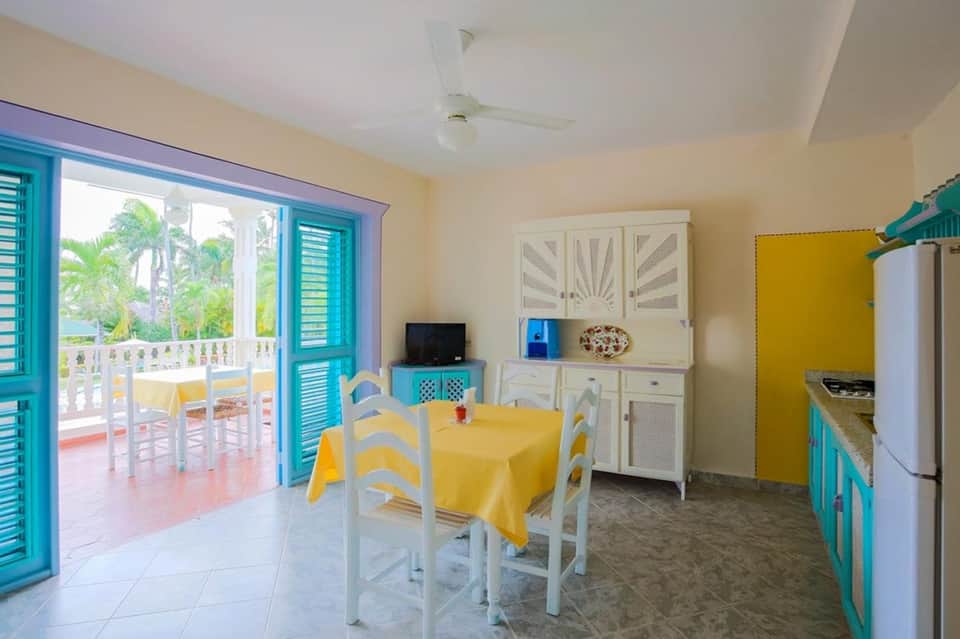 Colorful kitchen-dining room with turquoise doors, yellow table, white cabinetry, and patio view