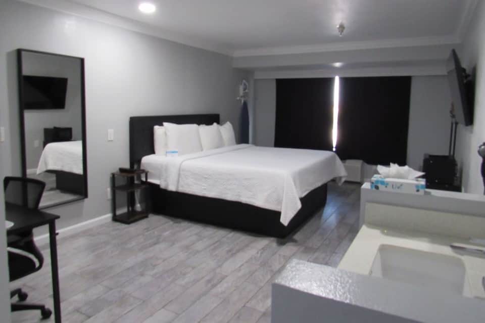 Modern hotel bedroom with king bed, black frame, gray flooring, large windows, mirror, and contemporary furnishings