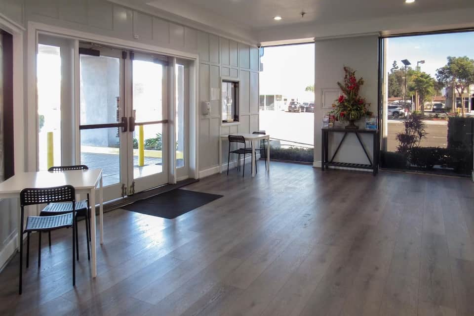 Bright hotel lobby with glass doors, wood flooring, and ocean view access
