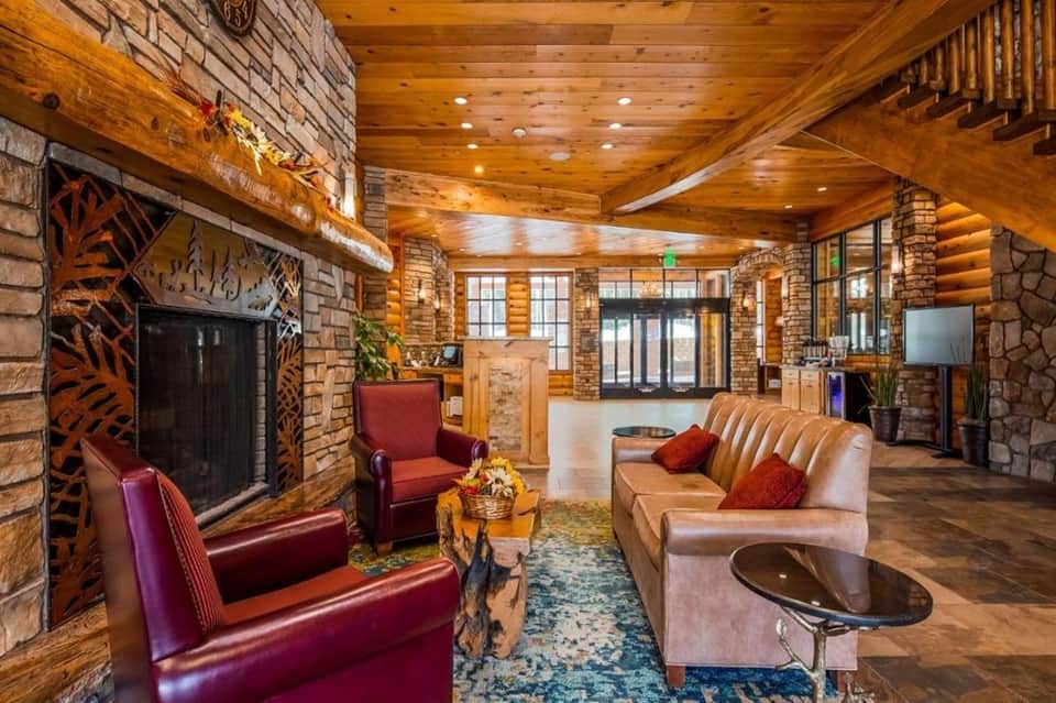 Rustic lodge lobby with stone fireplace, wooden beams, leather seating, and warm lighting