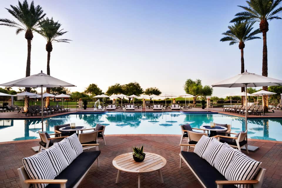 Luxurious resort pool surrounded by palm trees, lounge chairs, and large umbrellas at dusk