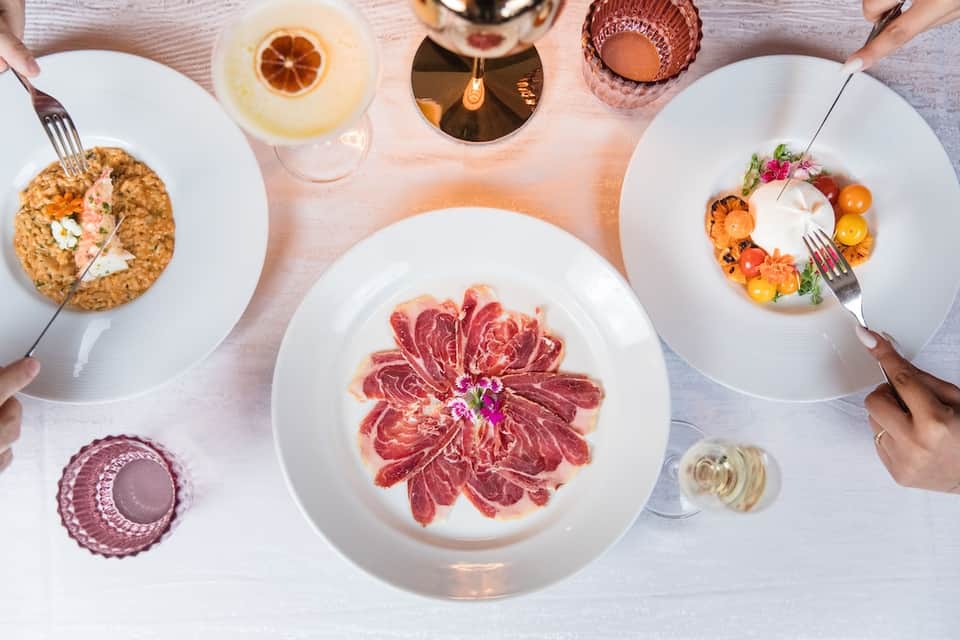 Fine dining overhead view with plated appetizers, cured meats, wine glasses, and elegant table setting