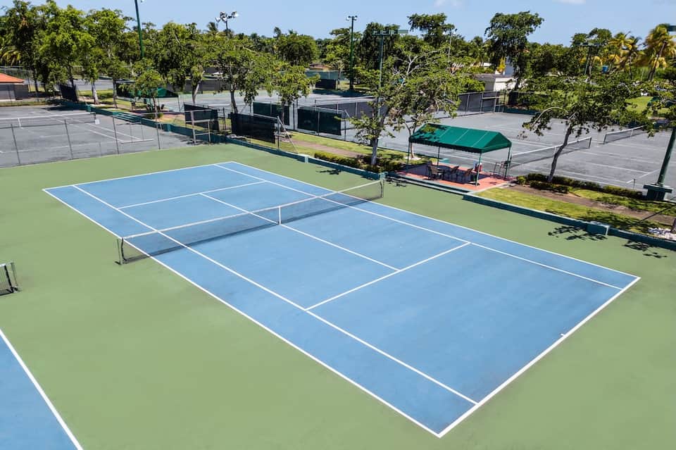 Tennis courts with blue and green surfaces, net, trees, and additional courts in background
