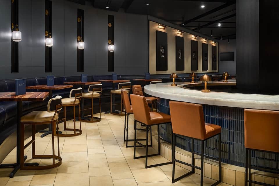 Contemporary bar lounge with copper bar stools, pendant lights, dark walls, and seating booths