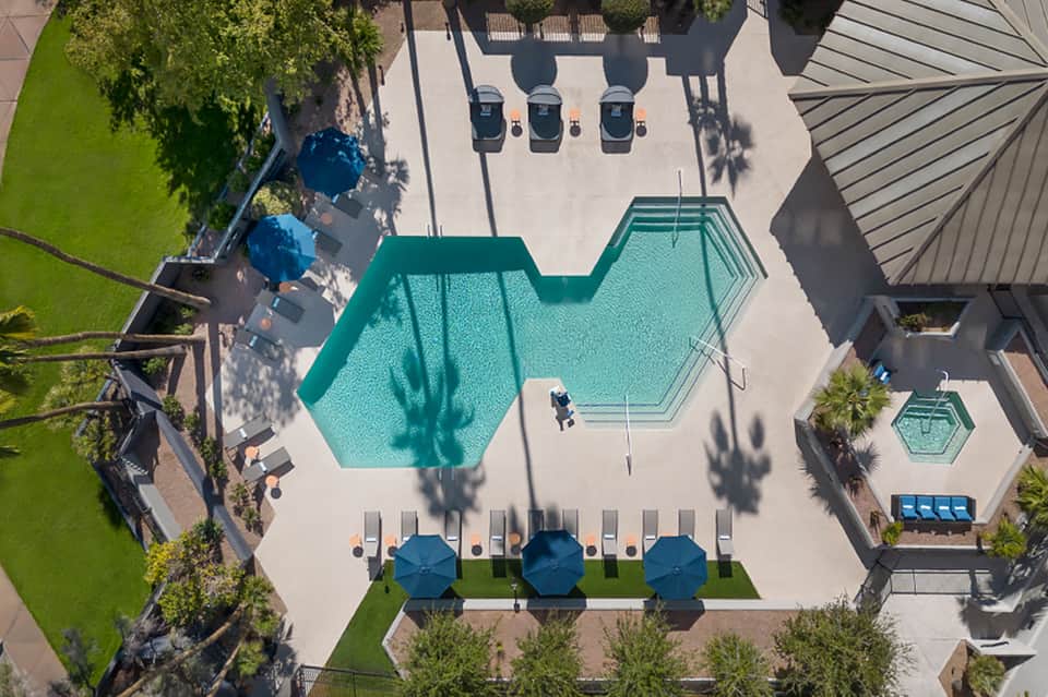 Aerial view of resort pool complex with hexagonal pools, umbrellas, lounge chairs, and landscaping