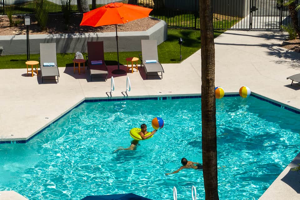 Children playing in bright turquoise resort pool with colorful umbrellas and beach loungers