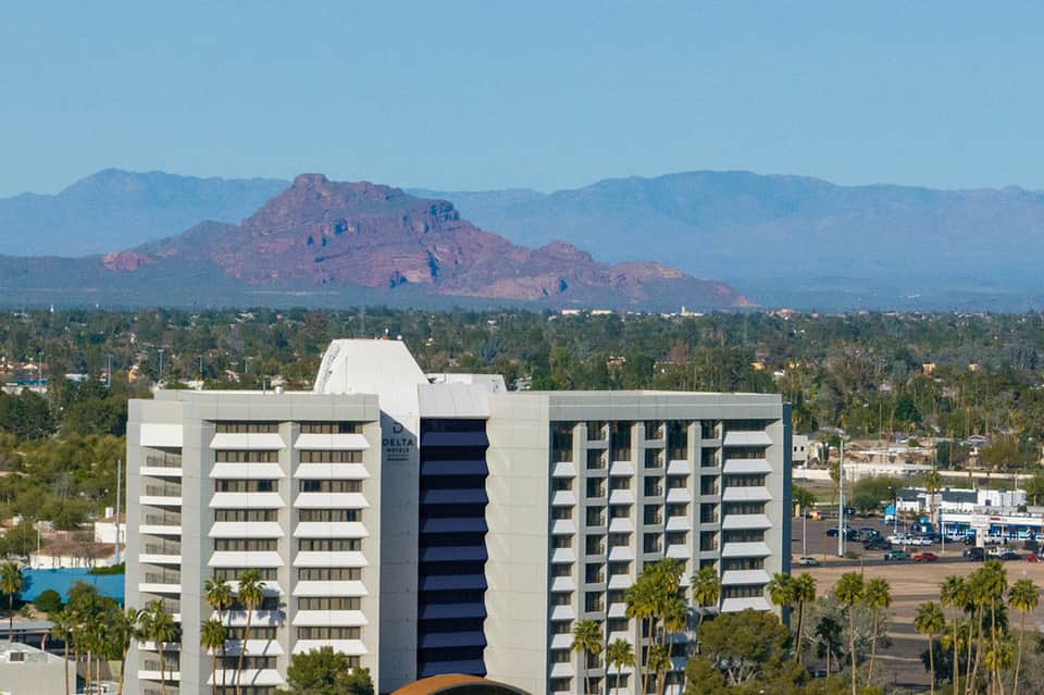 Multi-story resort hotel with mountains visible in background and palm tree landscaping