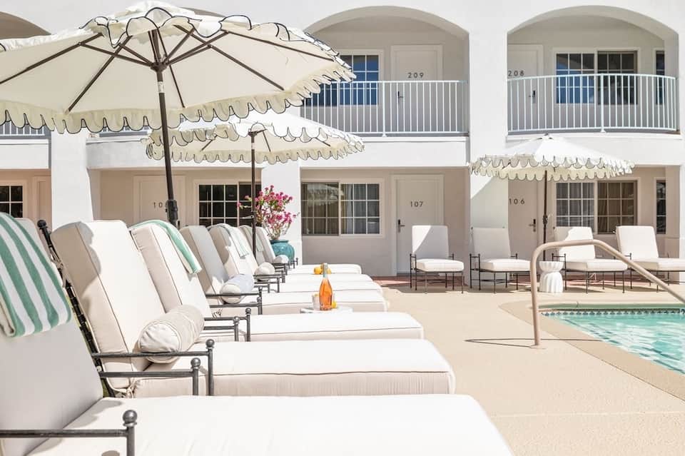 Elegant poolside lounge with white umbrellas, cushioned chairs, and whitewashed coastal buildings