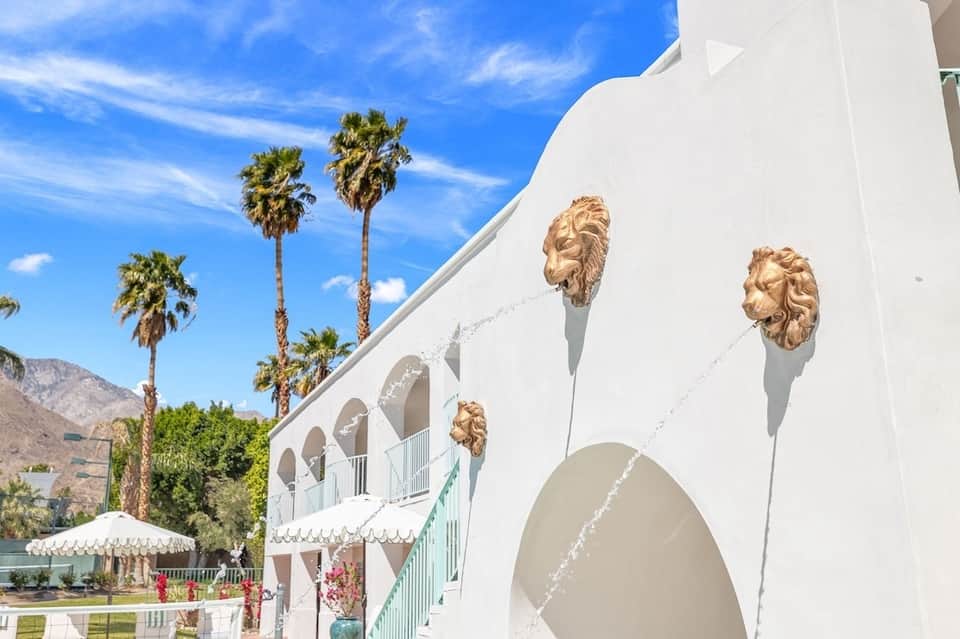 Luxurious white resort building with golden lion head sculptures, palm trees, and mountain landscape backdrop