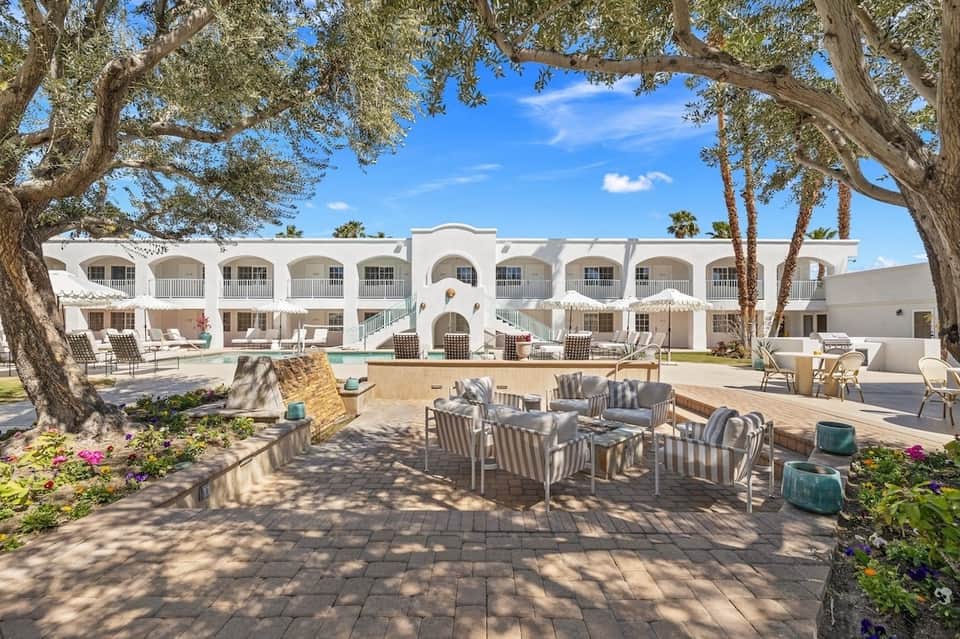Resort courtyard with white building, swimming pool, lounge chairs, and mature trees
