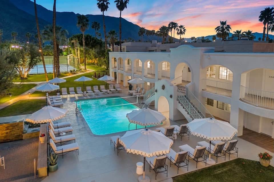 Desert resort with illuminated swimming pool, umbrellas, lounge chairs, and mountain backdrop at dusk