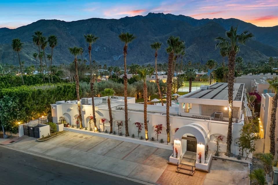 Illuminated modern white resort building at dusk with palm trees and mountain views