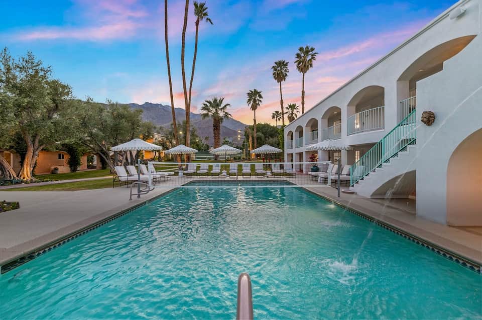 Elegant resort pool at sunset with white architectural arches, palm trees, and lounge chairs