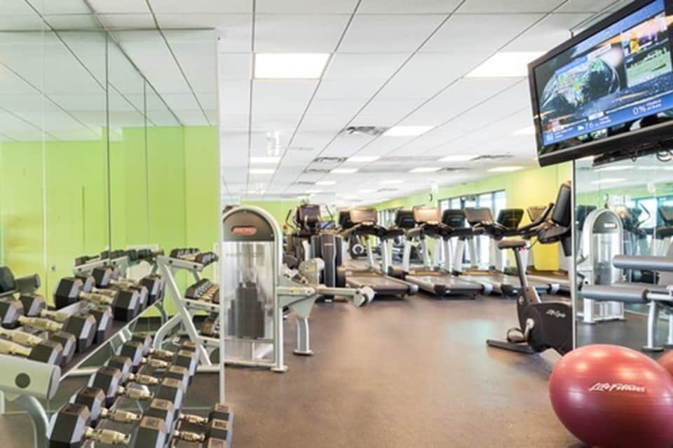 Modern fitness center with bright green accent walls, cardio equipment, dumbbells, and TV monitor
