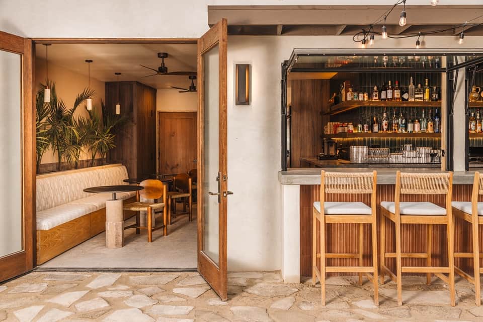 Wooden bar with seating area and lounge corner featuring palm plant and ambient lighting