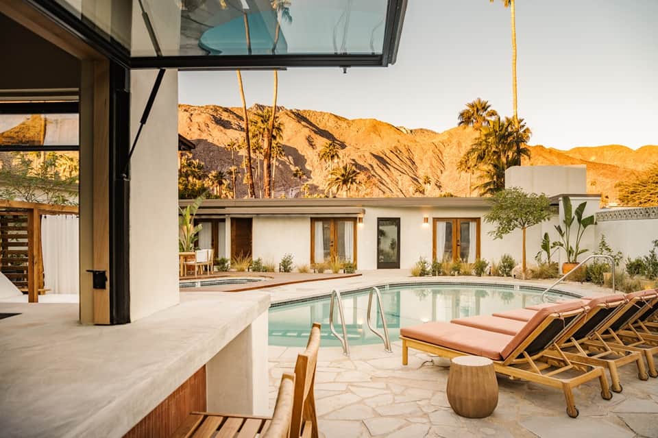 Desert resort pool area with modern architecture, mountain views, wooden lounge chairs, and spa-like amenities