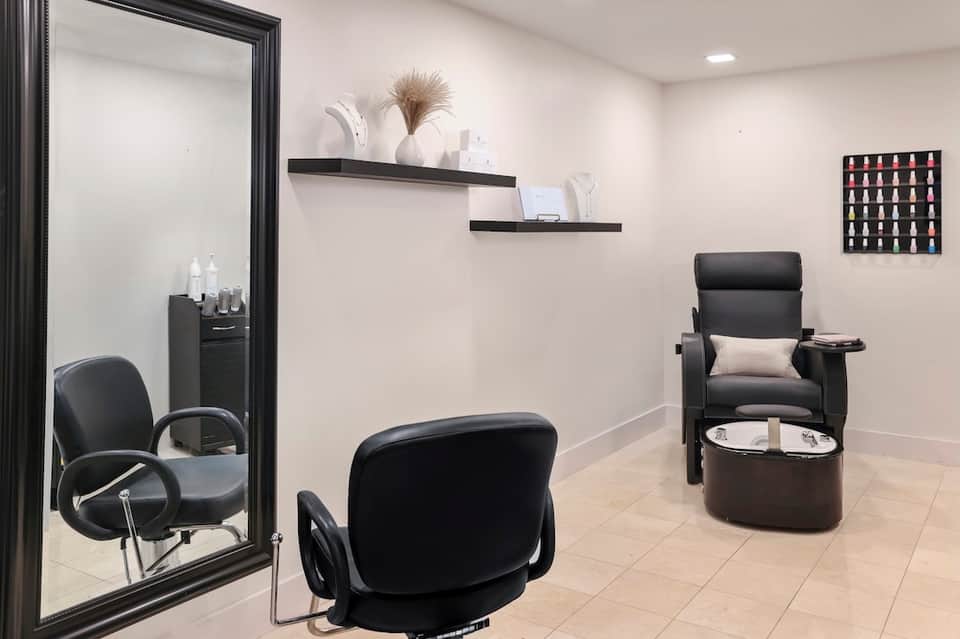 Spa pedicure room with black styling chair, footbath, mirror, shelving with products, and nail display