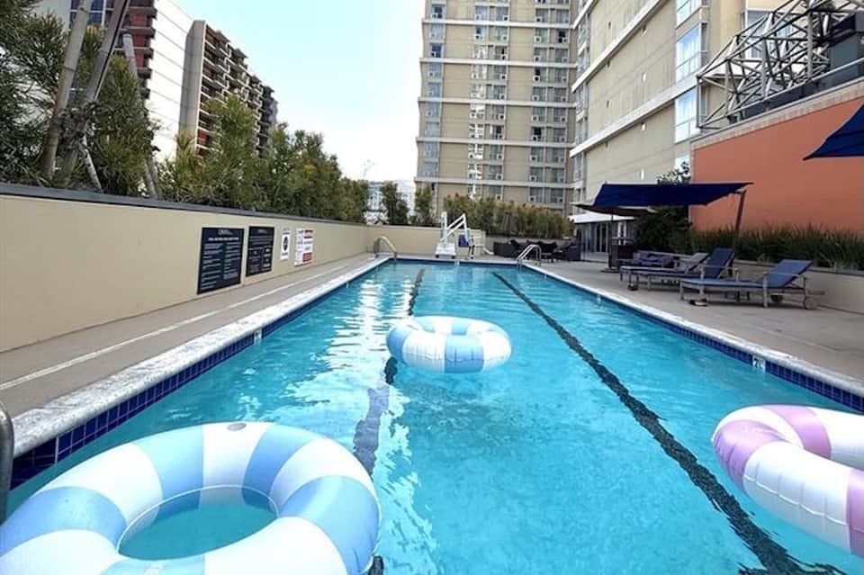 Resort lap pool with inflatable pool floats and blue loungers in urban setting