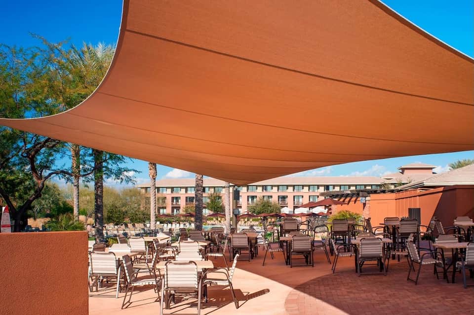 Outdoor patio with orange shade sail, palm trees, and desert resort setting