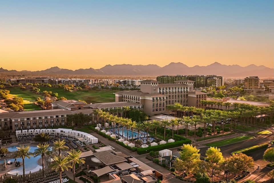 Aerial sunset view of sprawling resort with multiple pools, manicured grounds, and mountain backdrop