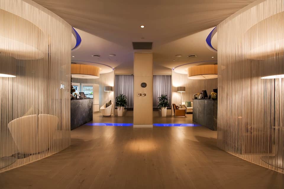Modern hotel lobby with dual reception desks, wood paneling, blue accent lighting, and minimalist contemporary design