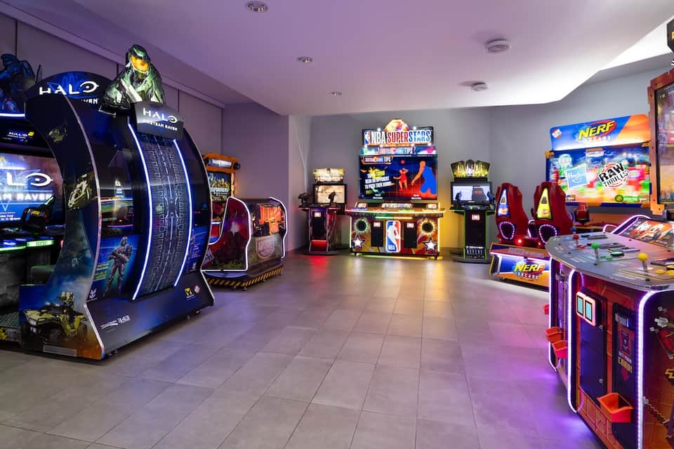 Game room with arcade machines including Halo and NBA games, colorful lighting and neon signs