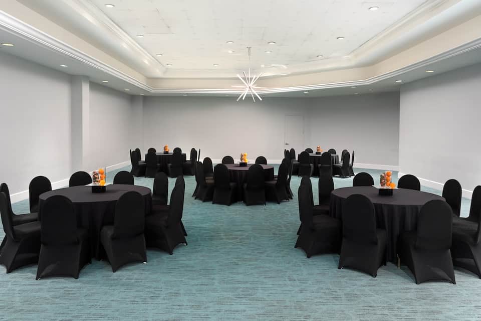 Banquet room with round tables covered in black linens, turquoise carpet, and recessed ceiling lights