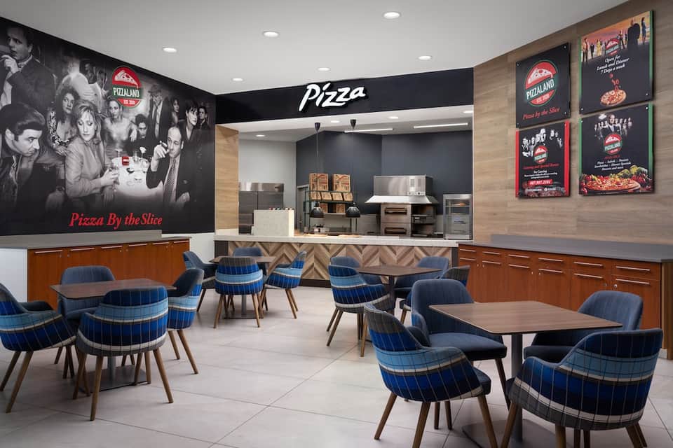 Modern Pizza by the Slice restaurant interior with counter service, kitchen, retro signage, and blue plaid seating