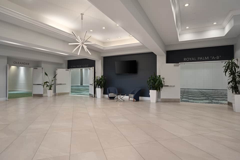 Bright hotel lobby with high ceilings, modern chandelier, and meeting room entrances
