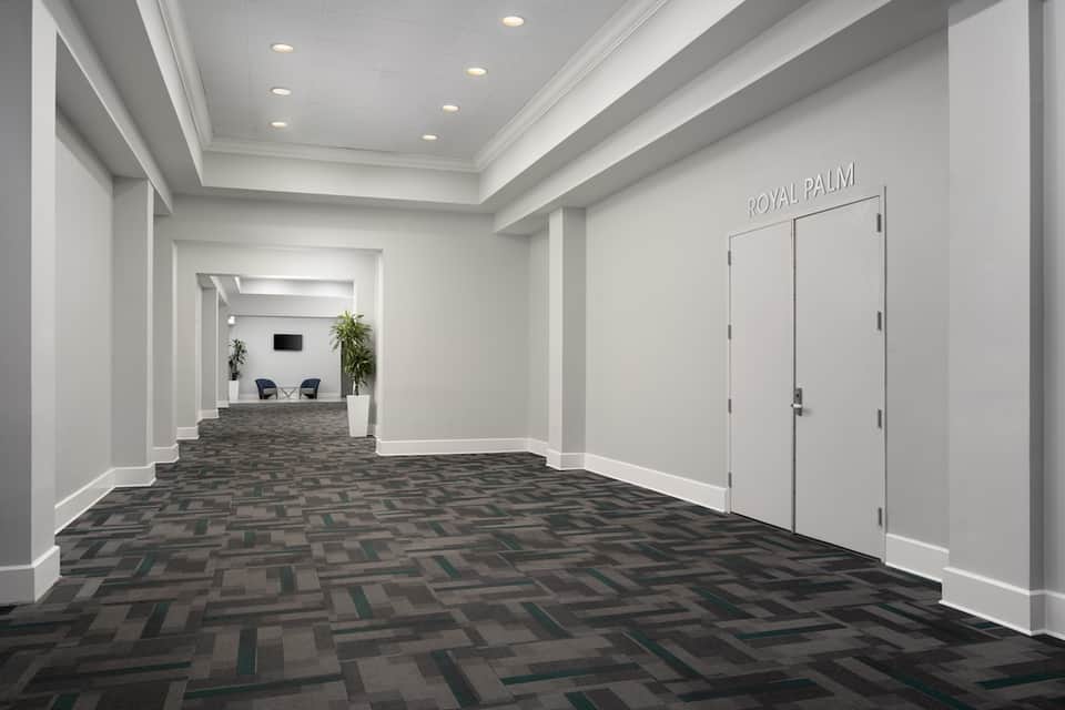 Modern hotel hallway with geometric floor pattern, white walls, recessed lighting, and Royal Palm signage