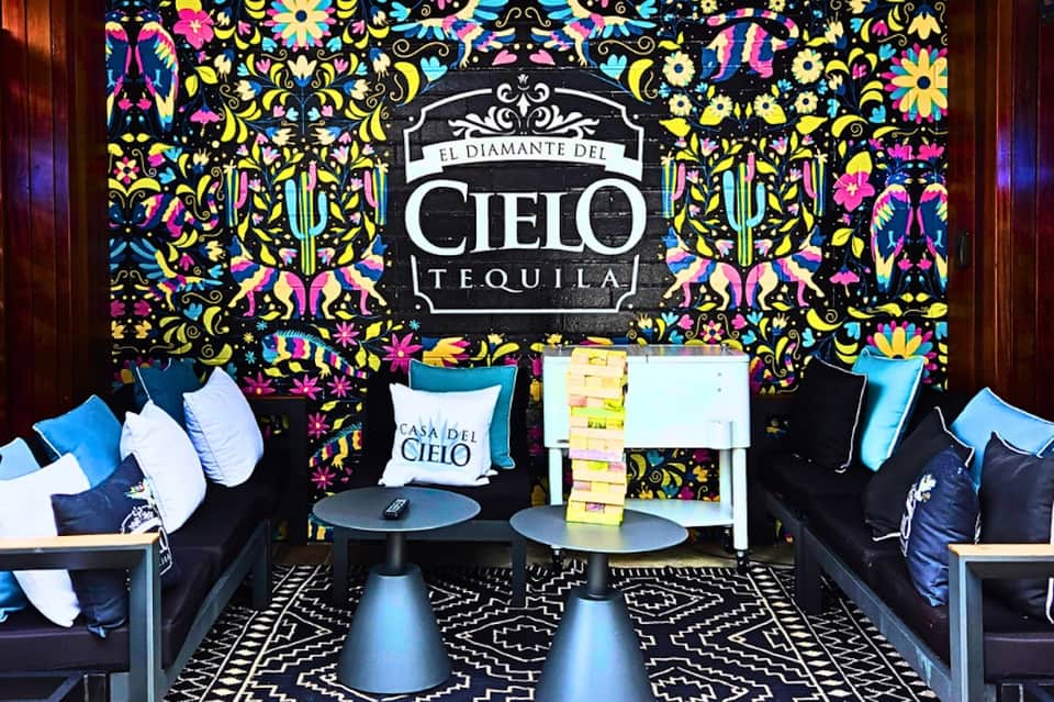 Vibrant lounge space with colorful floral wallpaper, El Diamante del Cielo Tequila branding, blue seating, and decorative pillows