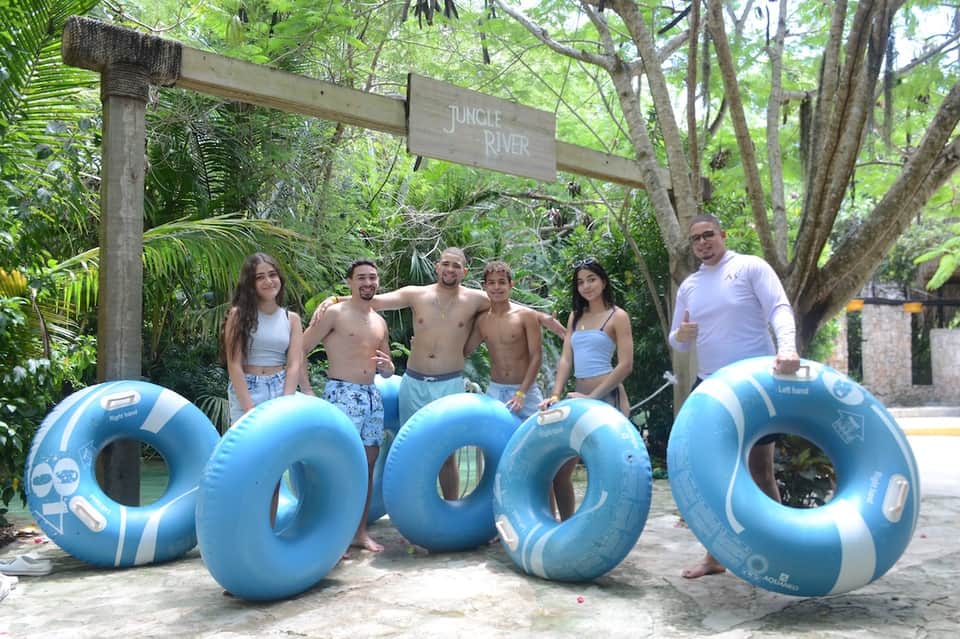 Group of six people with floats at jungle river attraction entrance surrounded by lush tropical trees